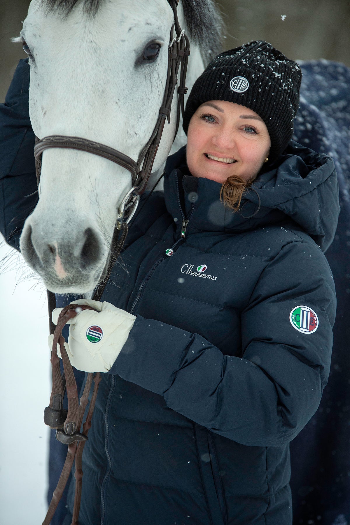 Rytter i marineblå C2E vinterjakke og lue sammen med en hvit hest i snøen
